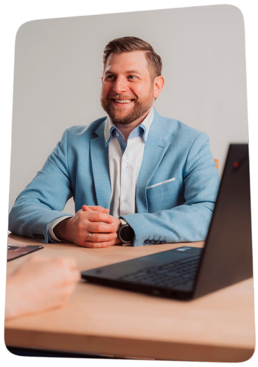 Stephan Trippl sitzend in einem hellblauen Anzug. Davor steht ein Notebook auf dem Tisch